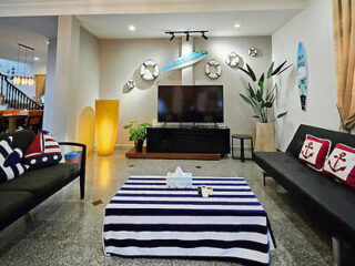 A modern living room with nautical decor, featuring a TV on a black stand, striped tablecloth, and cushions with anchor designs. Two surfboards are mounted on the walls as decoration.