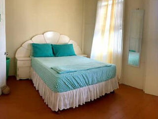 A bedroom with a double bed made up with turquoise and white bedding, two pillows, and a headboard. There is a small bedside table on the left, and a tall mirror on the wall to the right.