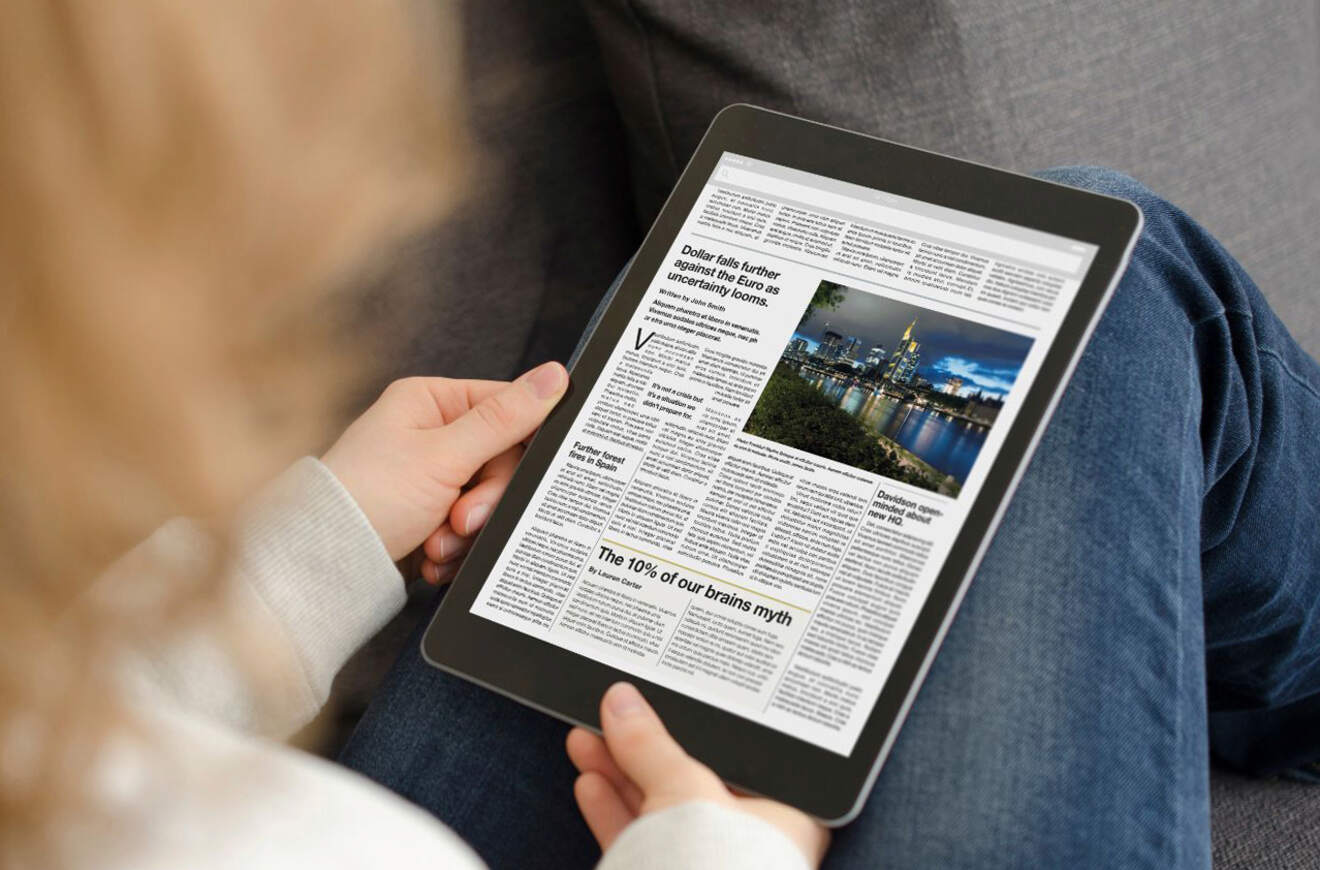 A person reads a digital newspaper on a tablet, focusing on an article about economic uncertainty.