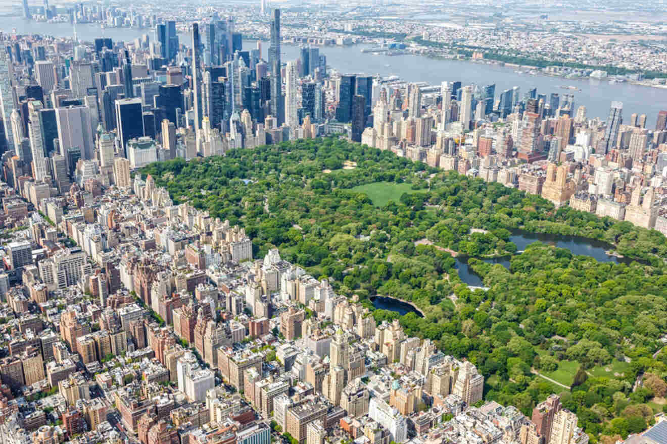 Aerial view of Central Park surrounded by the dense urban landscape of New York City with buildings, roads, and waterways visible.