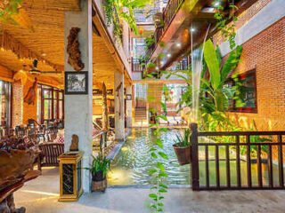 Indoor area of a building with water feature, wooden furniture, plants, brick walls, and multiple walkways. Bright lighting enhances the vibrant, nature-inspired decor.