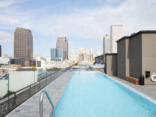 A rooftop pool with clear blue water overlooking a cityscape with various skyscrapers and buildings under a partly cloudy sky.