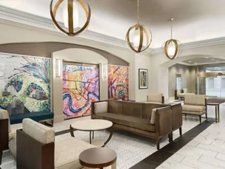A modern lobby area featuring contemporary seating, circular tables, large colorful abstract paintings, and three spherical pendant lights hanging from the ceiling.