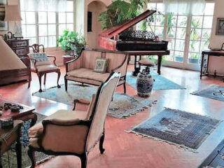Elegant sitting room featuring a grand piano, antique furniture, and large windows.