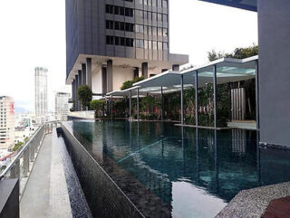 Rooftop infinity pool with a view of a city skyline. Modern high-rise buildings and a covered lounging area are in the background.