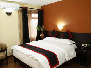 A comfortable bedroom with a rich orange accent wall, white bedding, and red and black pillows.