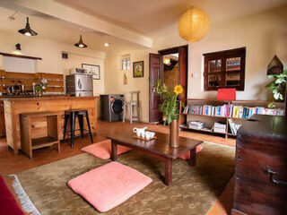 A cozy living area with low wooden tables, floor cushions, and a compact kitchen with rustic charm.
