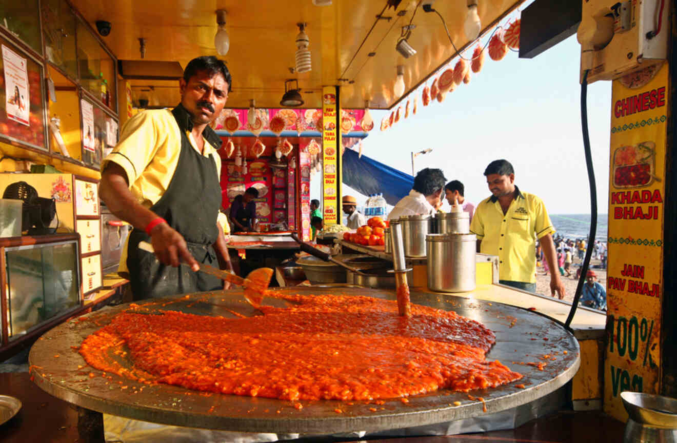 Street vendor cooking a large pan of pav bhaji at a vibrant market in Mumbai, India.