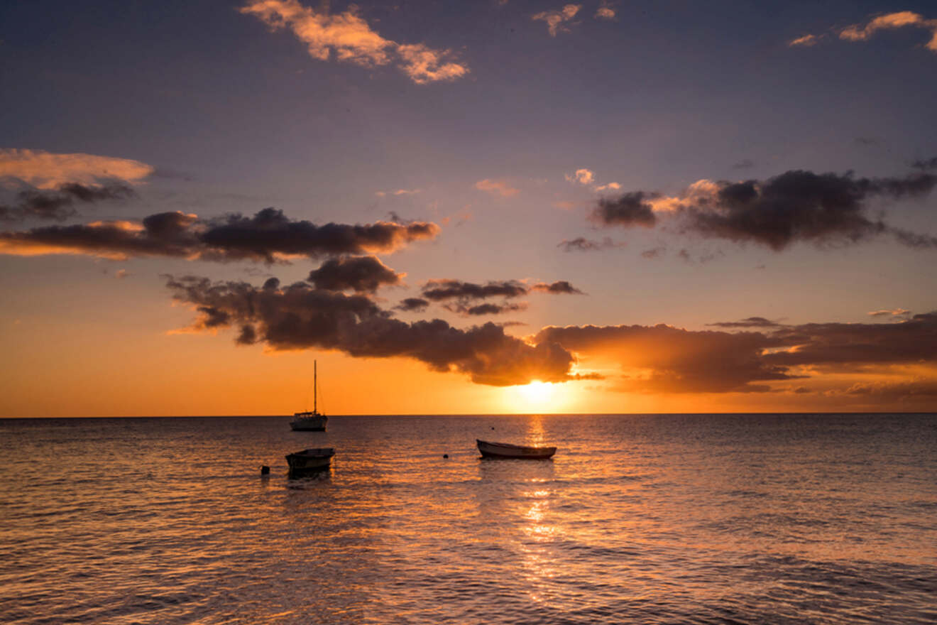 Three boats float on calm water under a vibrant sunset with scattered clouds in the sky.
