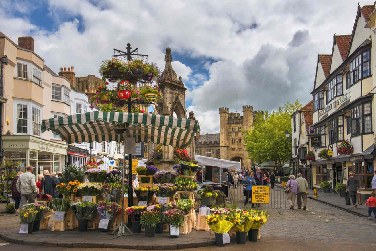 A colorful market scene with a variety of flowers for sale and a medieval building in the background.