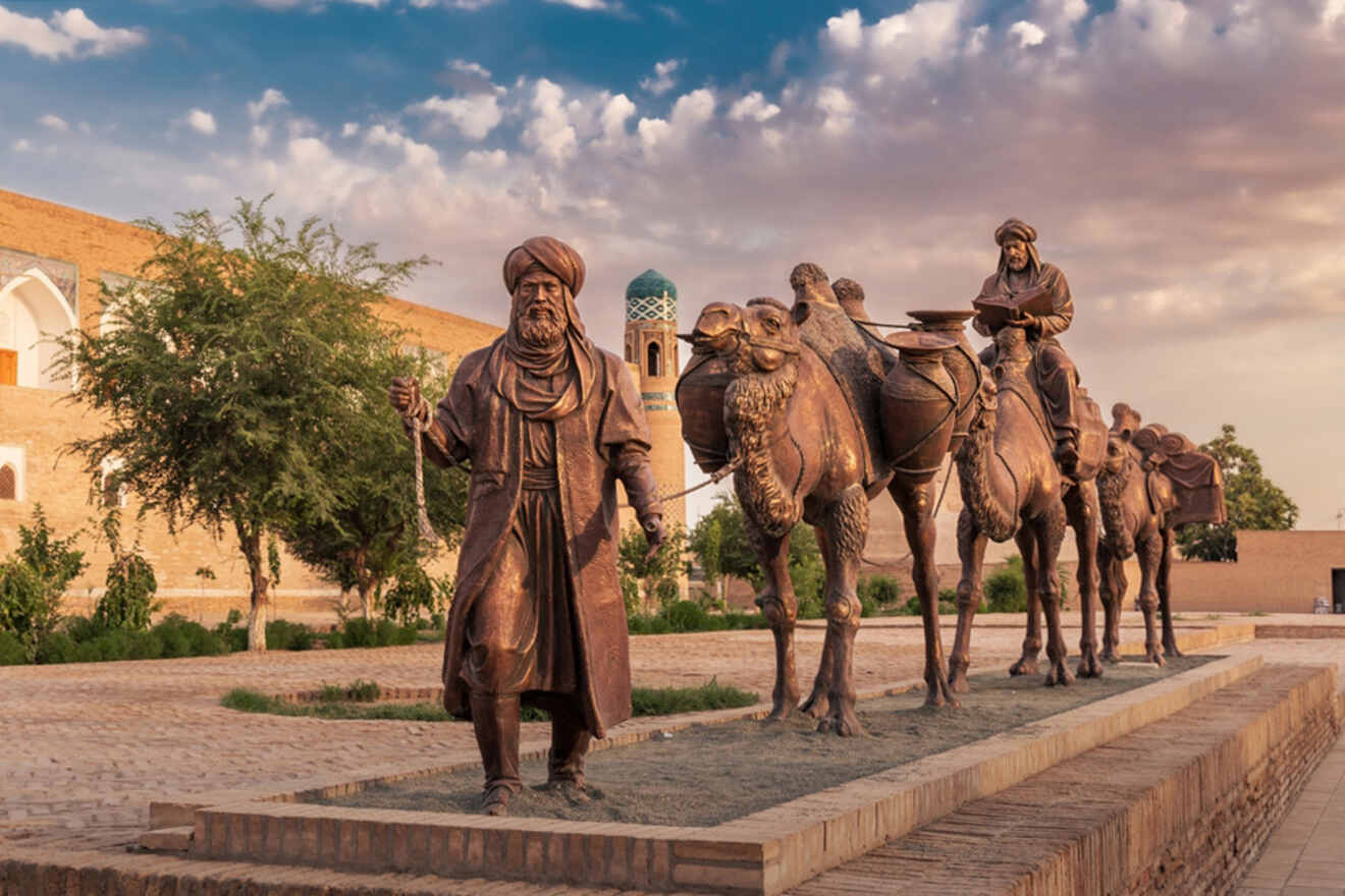 Bronze statue of a caravan leader and camels on the Silk Road, set against a backdrop of historic architecture and a blue sky with clouds.