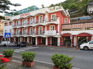 A three-story pink and white building with balconies labeled "Hotel Zeffiro." Cars are parked in front, and a street with a pedestrian crossing runs in front of the hotel.