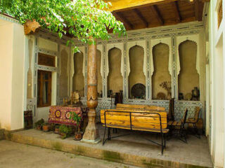 A traditional patio with ornate wooden columns, a decorative tablecloth, and lush green surroundings.