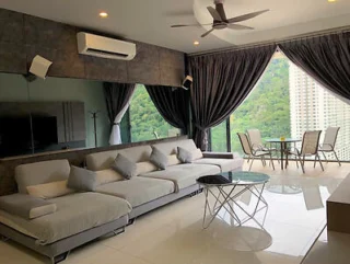 Modern living room with a large sectional sofa, glass coffee table, mounted TV, and floor-to-ceiling windows with dark curtains. A small dining area with table and chairs is set near the windows.