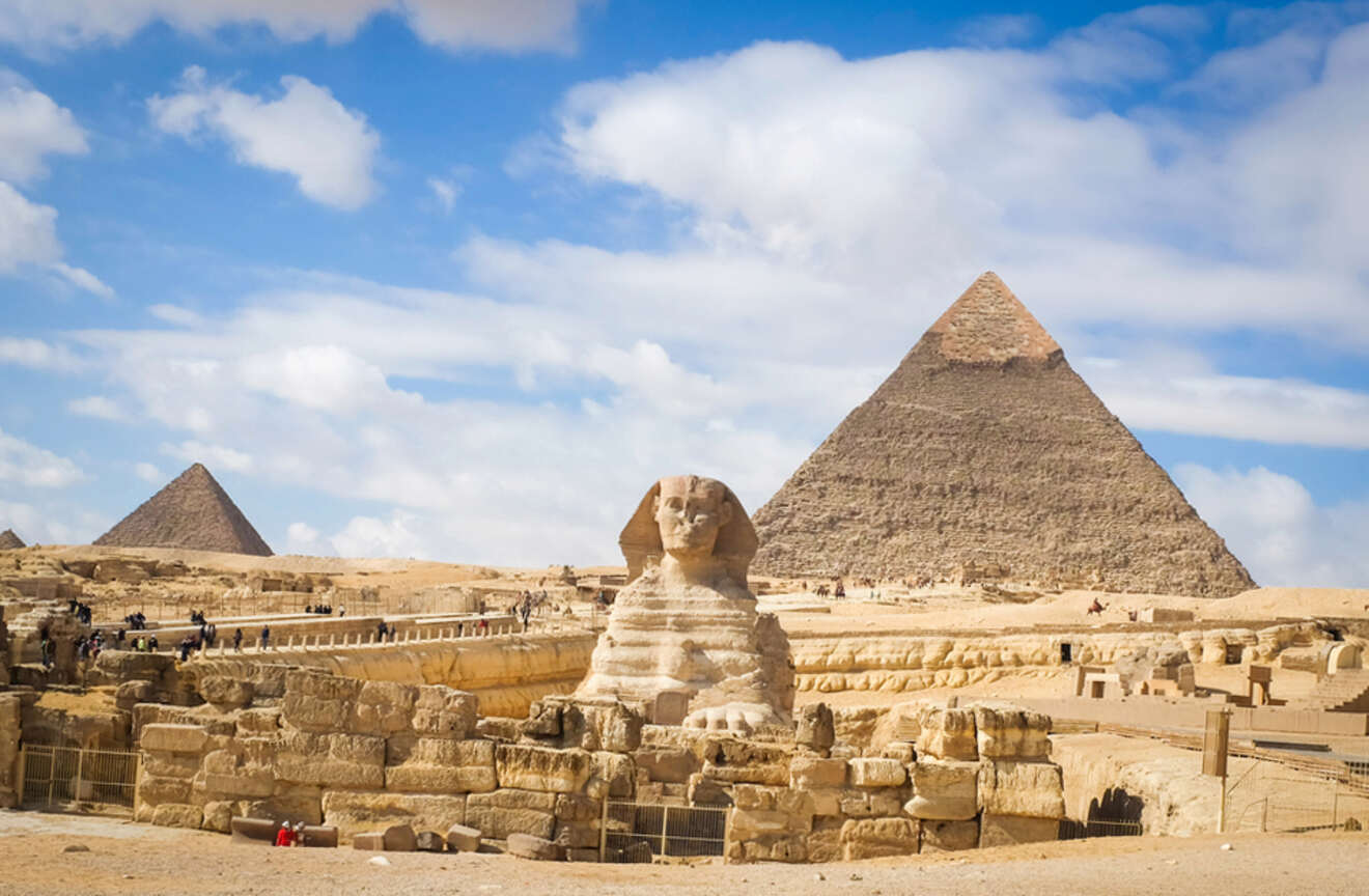 The Sphinx and the Pyramids of Giza with a bright blue sky and scattered clouds.