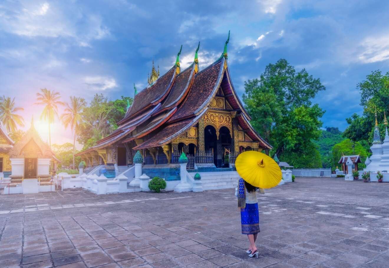 The serene Wat Xieng Thong temple in Luang Prabang, with its ornate golden roof and a woman holding a yellow umbrella.