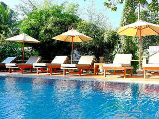 A serene poolside setting with sun loungers and umbrellas, surrounded by lush greenery.