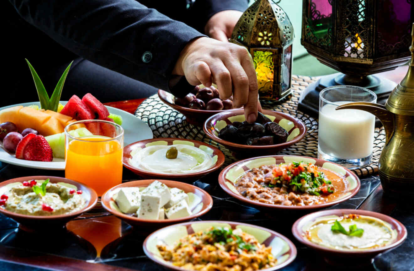 Hand reaching for dates among a variety of traditional dishes at an Iftar meal in Dubai, UAE.