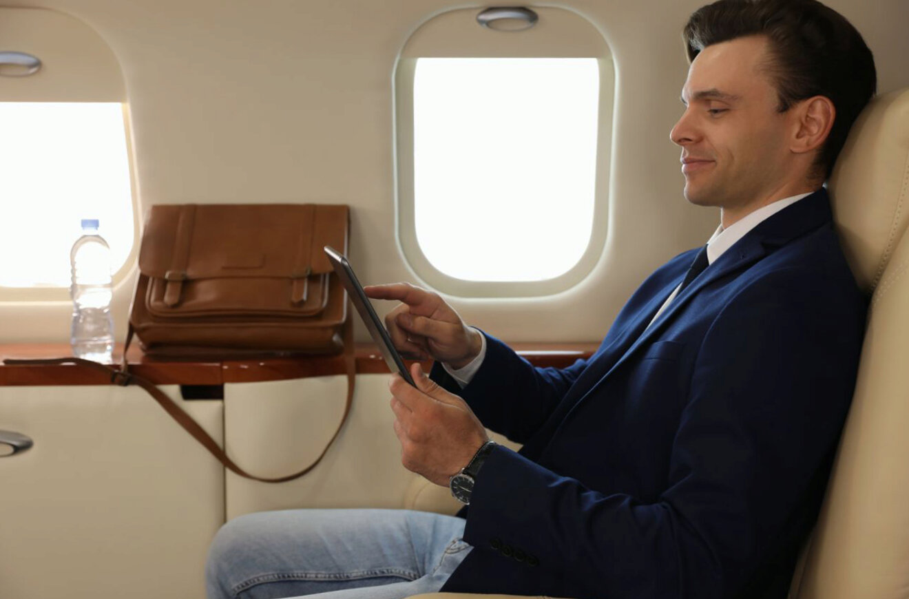 A man in a blue suit uses a tablet while seated in a well-appointed airplane cabin.