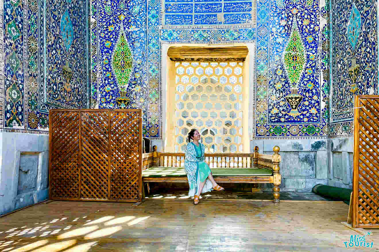 author of the post sits on a wooden bench in a room adorned with intricate blue and green tiled walls and a decorative golden door in the background.