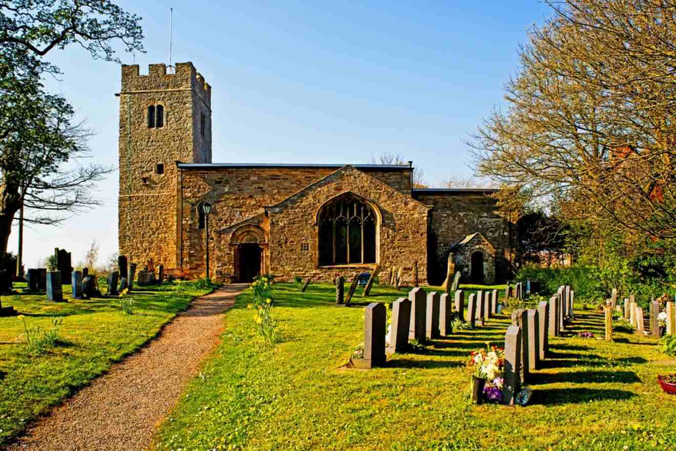 St. Cuthbert Church, a stone building with a tower, surrounded by a cemetery on a sunny day.