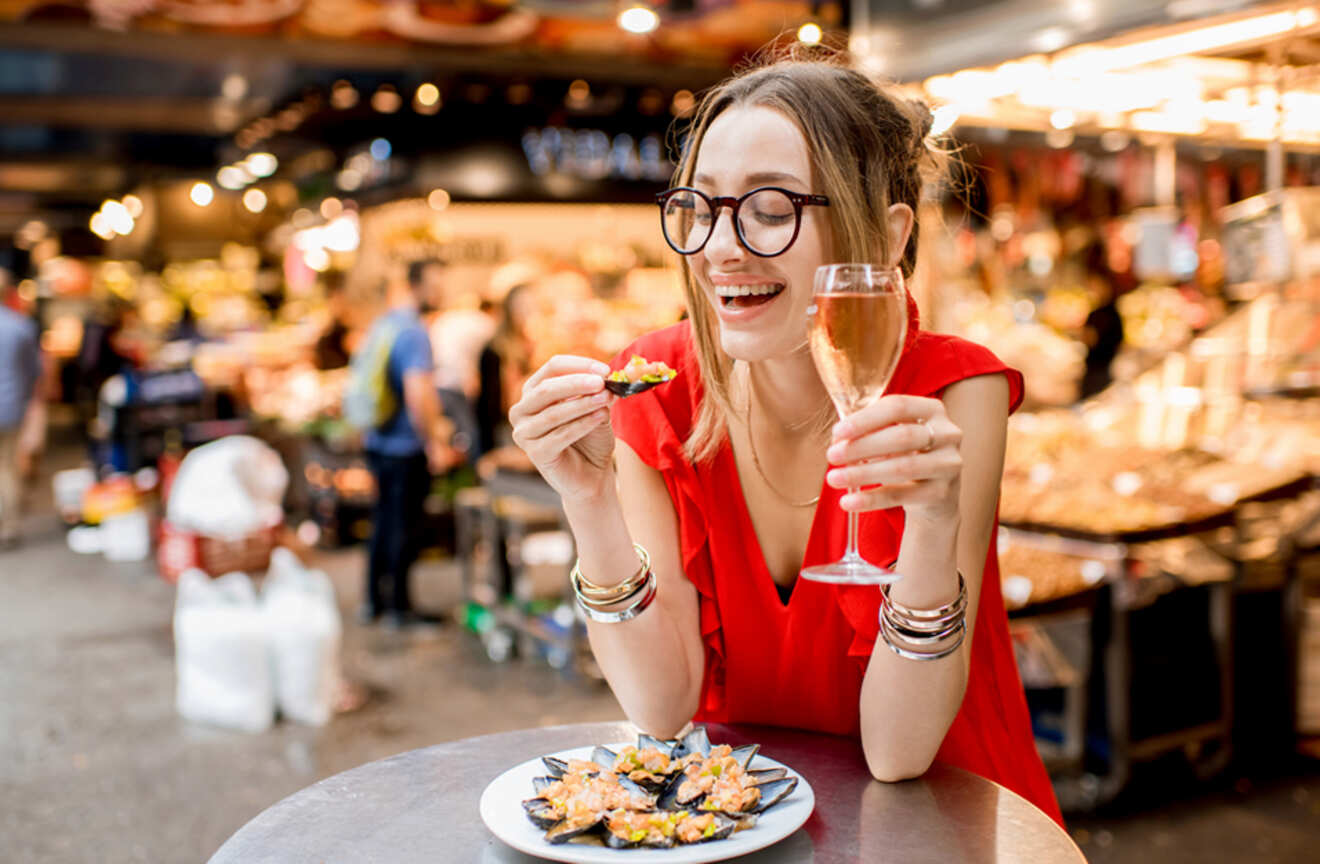 Woman in a red dress enjoying tapas and a glass of wine at a food market in Barcelona, Spain.