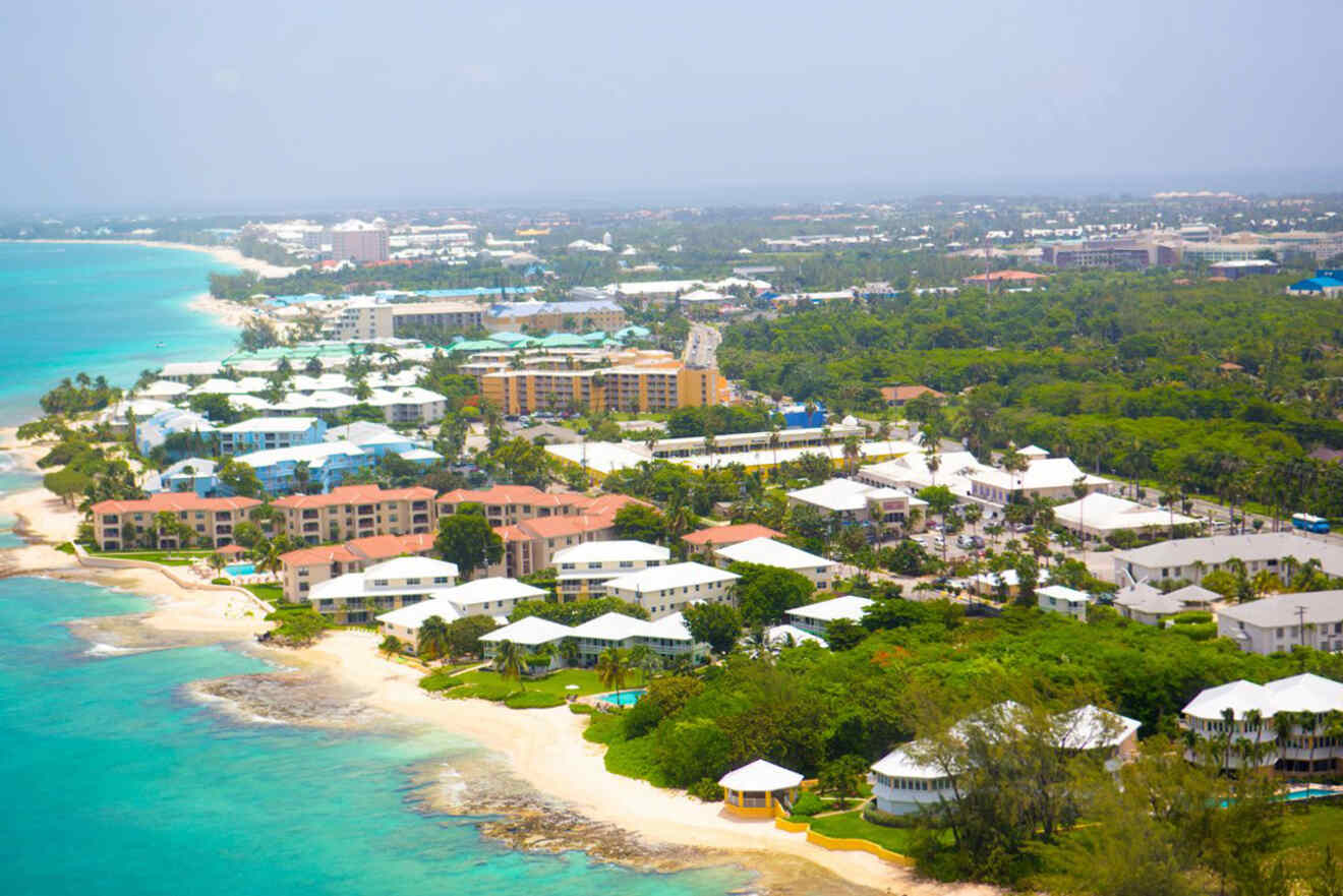 Aerial view of a coastal town featuring sandy beaches, beachfront homes, and lush green areas, with the ocean on the left and an array of buildings and trees stretching inland.