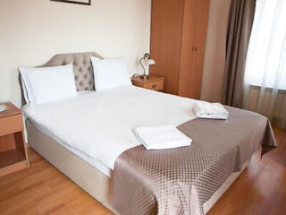 A neatly made double bed with white bedding, two pillows, and folded towels. The room has wooden furniture, curtains, and a window letting in natural light.