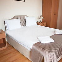 A neatly made double bed with white sheets and pillows, two folded towels on top, and bedside tables with lamps in a simple, tidy bedroom.