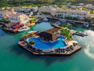 Aerial view of Port St. Charles resort in Barbados, showing a lagoon pool with swim-up bar surrounded by yachts, marina berths and waterfront villas.