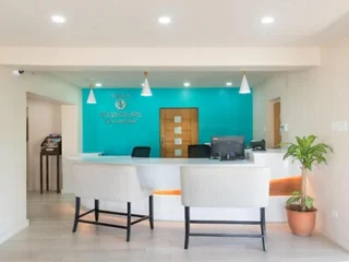 Reception desk at Rostrevor Hotel in Barbados, with a curved white counter against a turquoise feature wall, pendant lights and armchairs in the lobby.