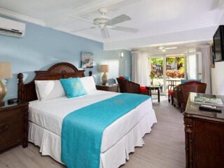 Guest room at The Club Barbados Adults Only All Inclusive, with a carved wooden bed, turquoise accents and French doors opening onto a garden patio.