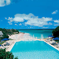 Swimming pool with lounge chairs overlooks a sandy beach and turquoise ocean under a blue sky with scattered clouds.