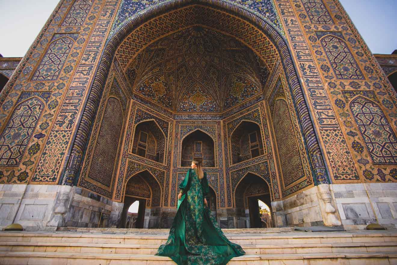 A person in a long, green dress stands in front of an intricately decorated, arched building entrance with colorful tiles.