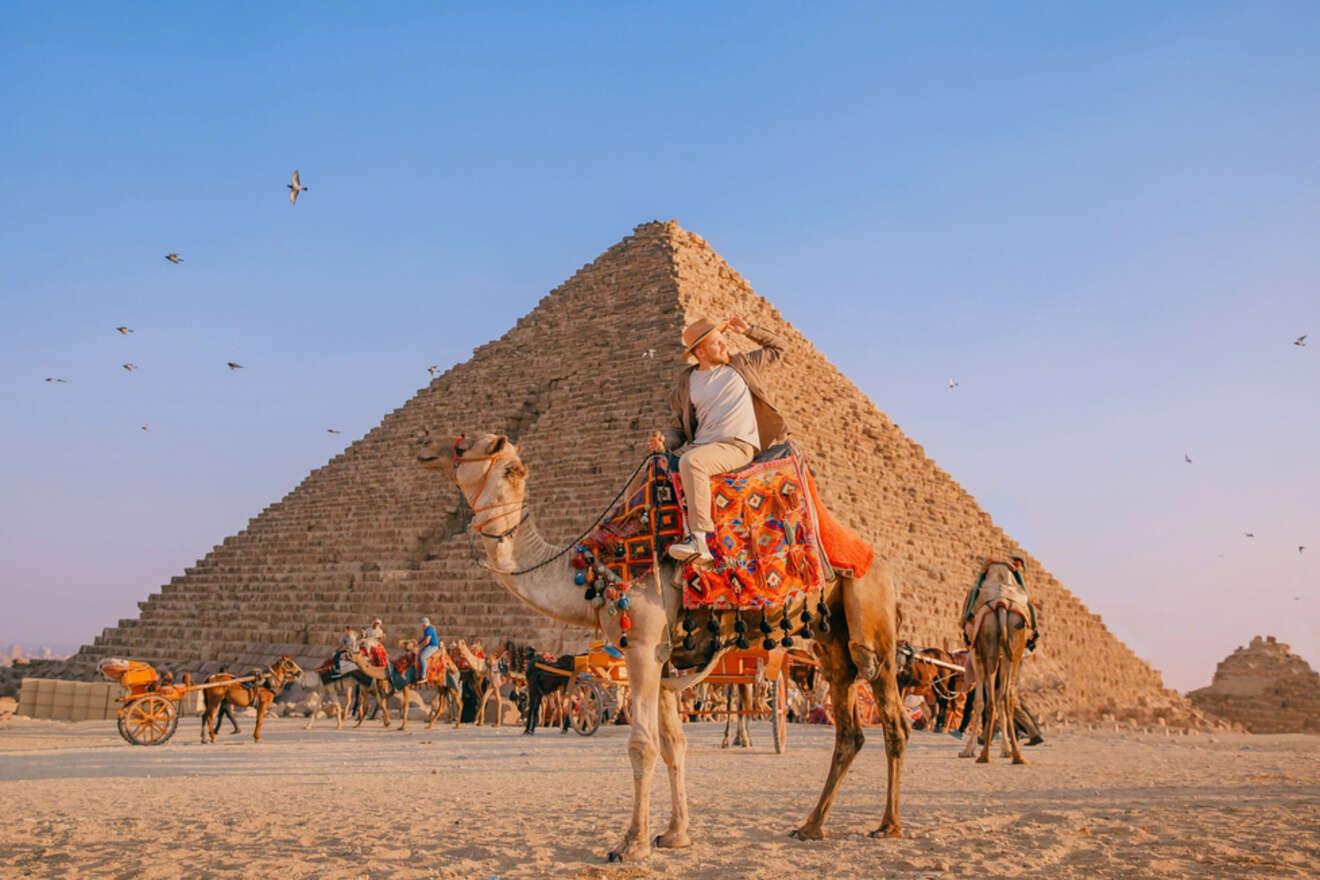 Tourists riding camels and horses in front of the Great Pyramid of Giza during sunset.