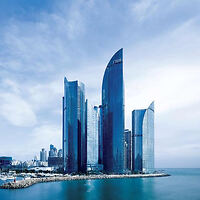 Modern skyscrapers with sleek, curved designs standing by the waterfront under a blue sky.