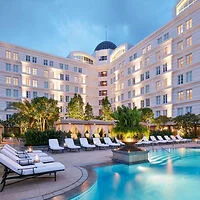 Luxury hotel with a grand facade, surrounded by illuminated windows, featuring an outdoor pool area lined with lounge chairs and greenery.