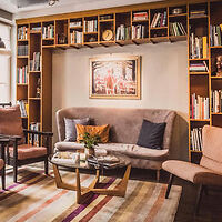 A cozy living room features a bookshelf, a central art piece, a sofa with cushions, armchairs, a glass coffee table, and a striped rug.