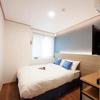 Cozy bedroom with a double bed, white bedding, and a small desk with a television. 