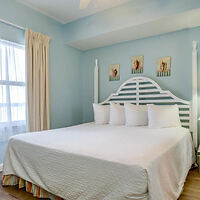 A simple bedroom with a large white bed, three white pillows, pale blue walls, light beige curtains, and three framed pictures above the headboard.