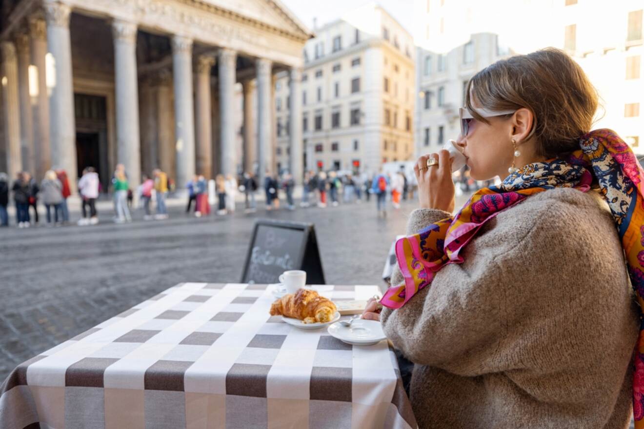 A person enjoying an espresso and croissant at a cafe with a view of the Pantheon in Rome.