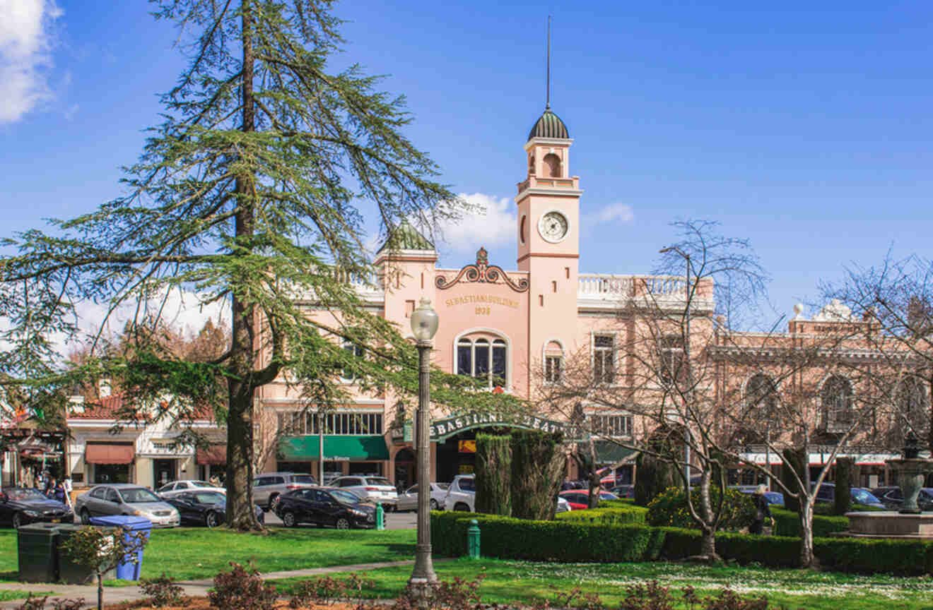 The Sebastiani Theatre building in Sonoma City with its distinctive clock tower and pink facade, surrounded by green trees and parked cars.