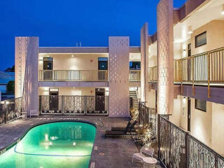 A modern apartment complex with two floors, featuring a central swimming pool and metal railings on the balconies and around the pool area, illuminated at dusk.