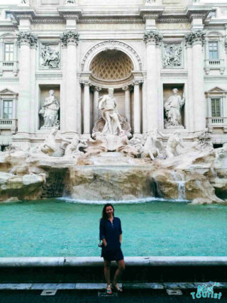 The writer of the post standing in front of the Trevi Fountain in Rome, with its grand sculptures and turquoise water.