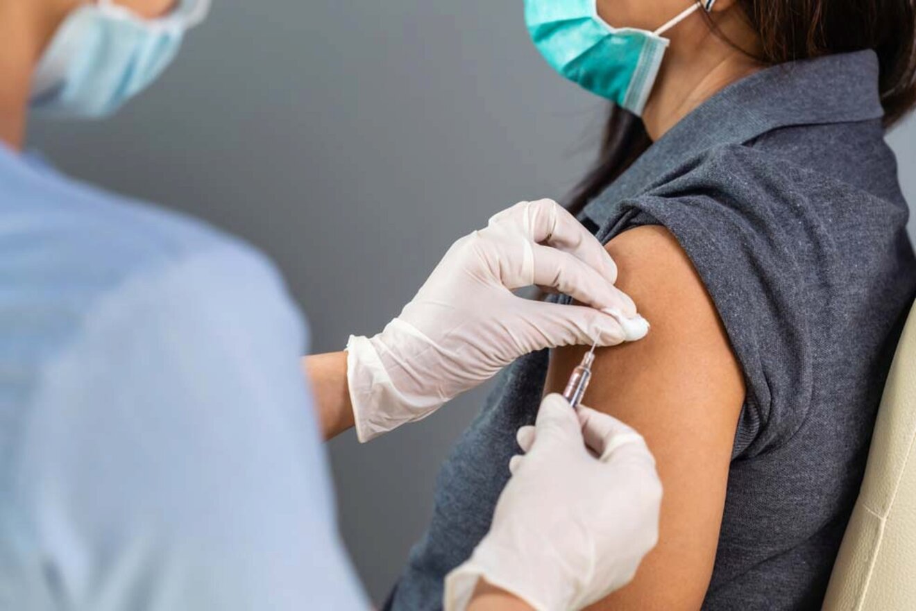 A person receives a vaccination shot in the arm from a healthcare worker wearing gloves and a mask.