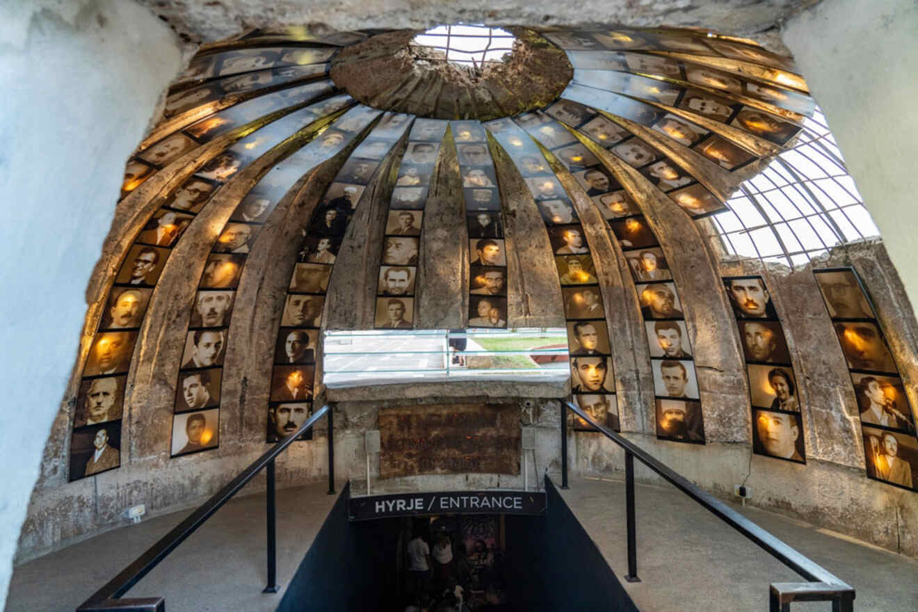 Interior view of a dome-shaped bunker museum in Tirana, with photographs of faces covering the walls and an entrance sign in the foreground.