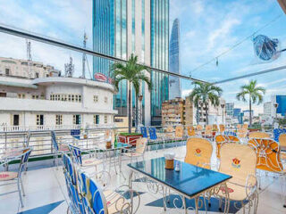 Rooftop terrace with tables and chairs, featuring cityscape views of tall buildings and palm trees in the background.