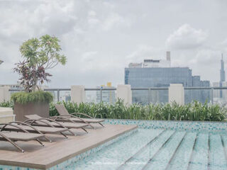 Rooftop pool with lounge chairs and potted plants overlooking a cityscape with tall buildings on a cloudy day.