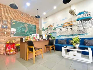 A cozy reception area with brick and mural walls, a wooden desk, two chairs, a blue couch, and a white coffee table. The area is decorated with plants and various items on the desk.