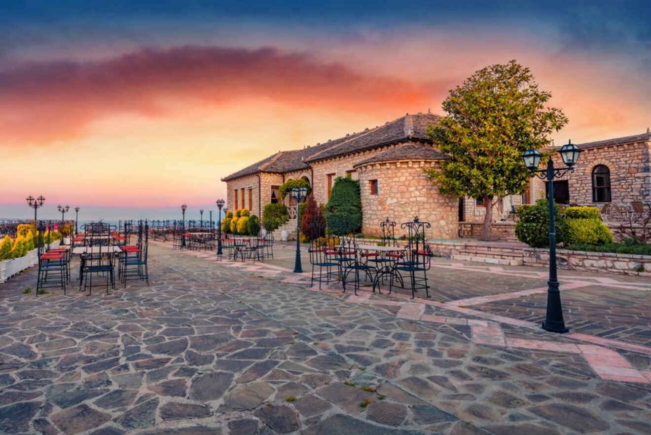 An outdoor terrace of Lekursi Castle at sunset, with empty tables and chairs set against a backdrop of stone buildings and a colorful sky.